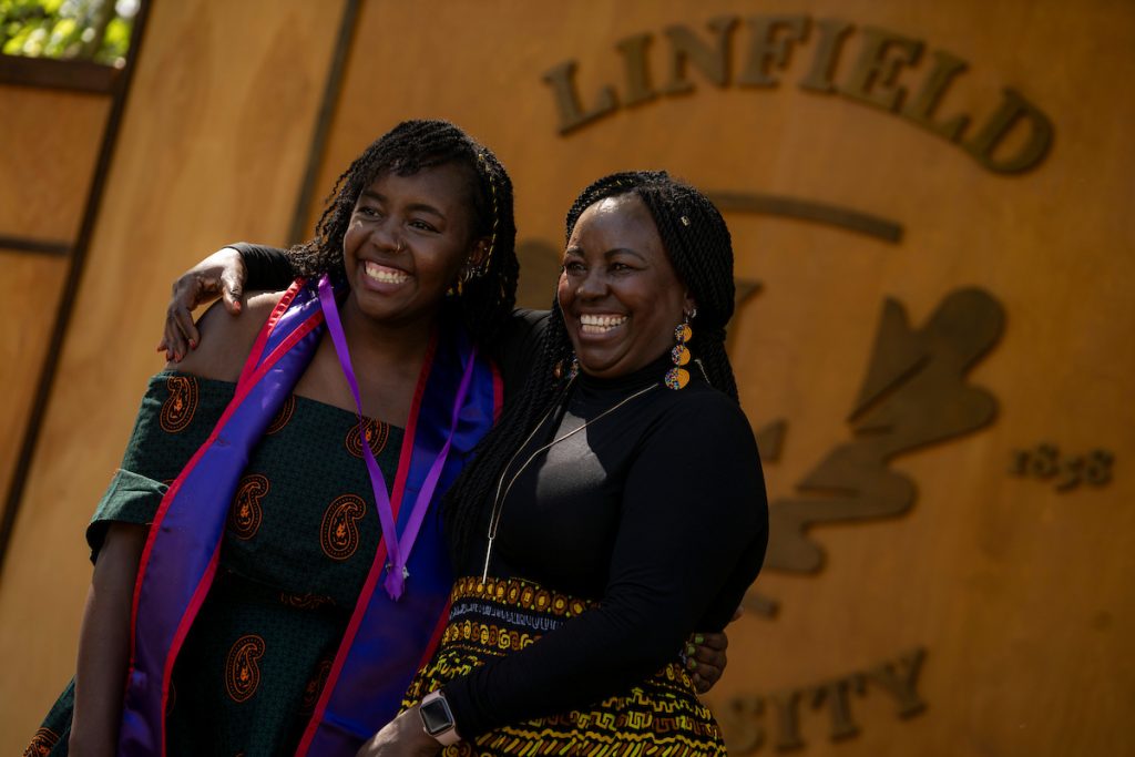 A family member places a purple stole with a red border around the neck of a Linfield University School of Nursing graduate.