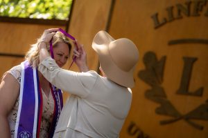 A family member places a purple stole with a red border around the neck of a Linfield University School of Nursing graduate.