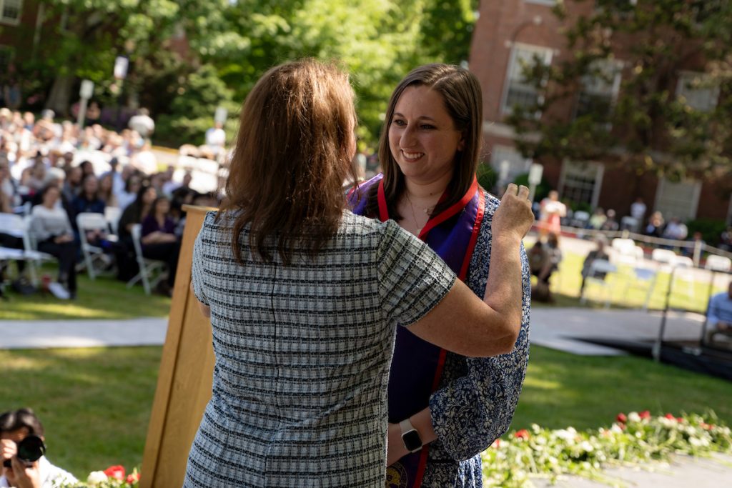 A family member places a purple stole with a red border around the neck of a Linfield University School of Nursing graduate.