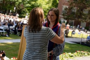 A family member places a purple stole with a red border around the neck of a Linfield University School of Nursing graduate.