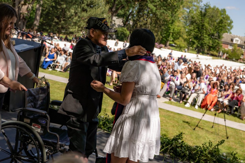 A family member places a purple stole with a red border around the neck of a Linfield University School of Nursing graduate.