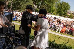 A family member places a purple stole with a red border around the neck of a Linfield University School of Nursing graduate.