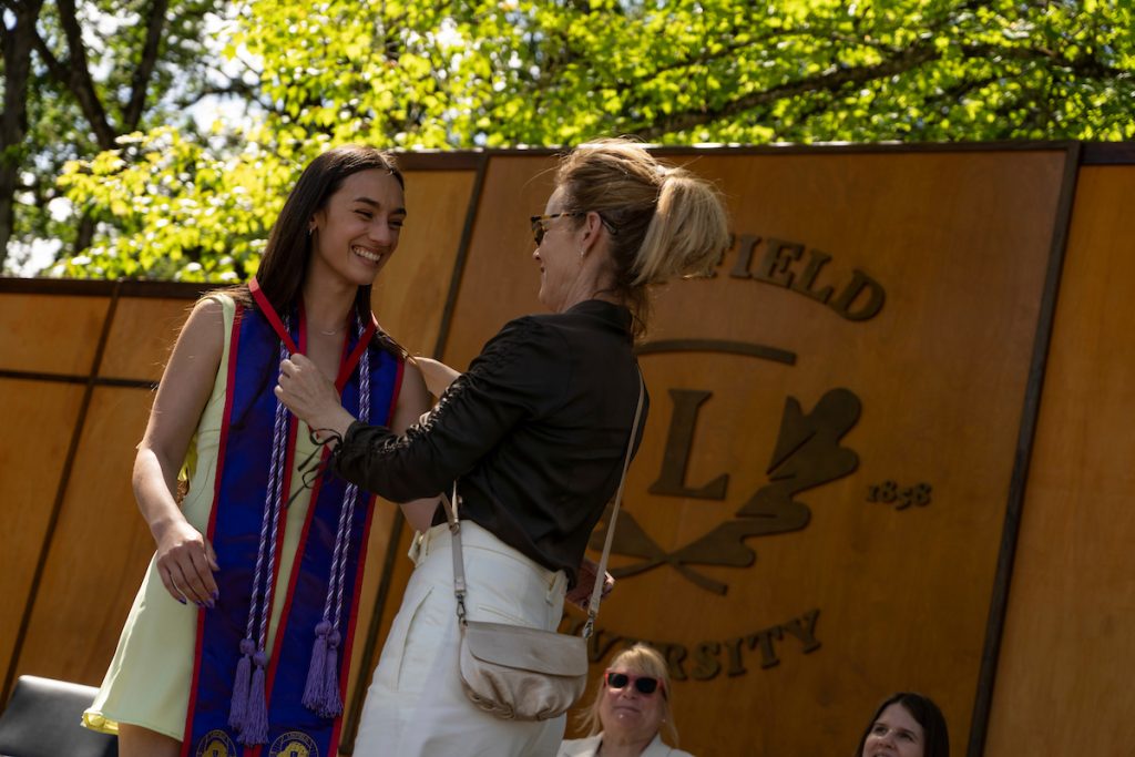 A family member places a purple stole with a red border around the neck of a Linfield University School of Nursing graduate.