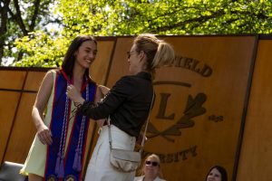 A family member places a purple stole with a red border around the neck of a Linfield University School of Nursing graduate.