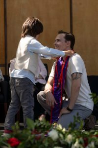 A family member places a purple stole with a red border around the neck of a Linfield University School of Nursing graduate.