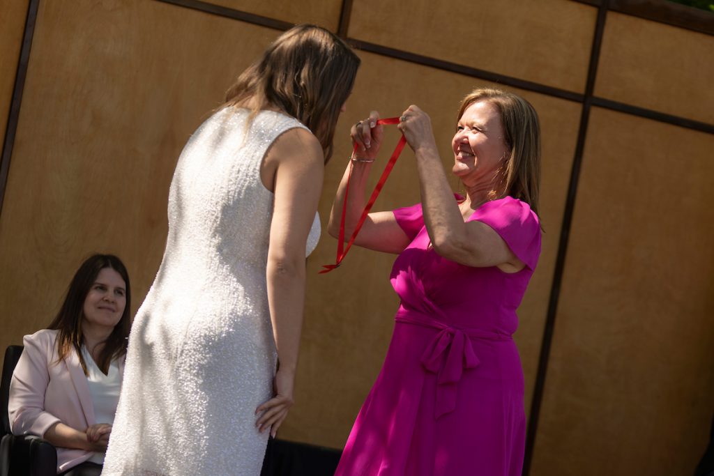 A family member places a purple stole with a red border around the neck of a Linfield University School of Nursing graduate.
