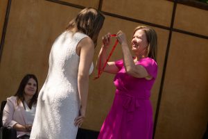A family member places a purple stole with a red border around the neck of a Linfield University School of Nursing graduate.