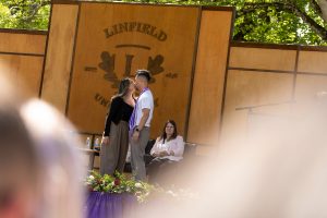 A family member places a purple stole with a red border around the neck of a Linfield University School of Nursing graduate.
