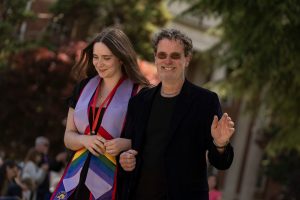A Linfield University School of Nursing graduate wears a lavender and rainbow stole and walks arm-in-arm with a loved one.
