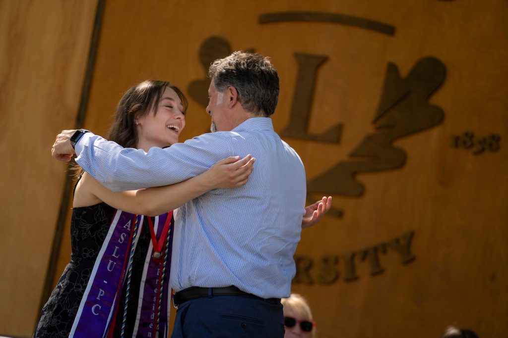 A family member places a purple stole with a red border around the neck of a Linfield University School of Nursing graduate.