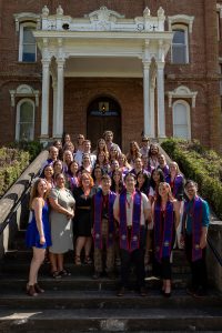 Graduates of the Linfield University School of Nursing stand on the steps of Pioneer Hall, each with a purple stole around their neck.