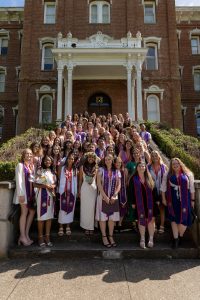 Graduates of the Linfield University School of Nursing stand on the steps of Pioneer Hall, each with a purple stole around their neck.