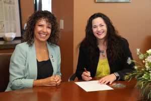 Two women sit at a table at COMP-Northwest, signing a memorandum of understanding. 