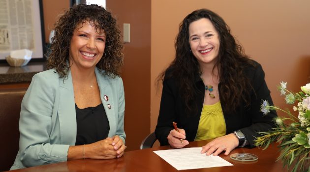 Two women sit at a table at COMP-Northwest, signing a memorandum of understanding.