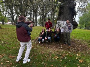Students pose in front of an oak tree with a Linfield University Majestic Tree Week banner.