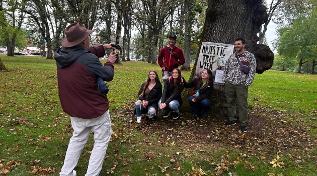 Students pose in front of an oak tree with a Linfield University Majestic Tree Week banner.
