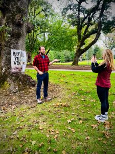 A man stands in front of an oak tree with a Linfield University Majestic Tree Week banner.