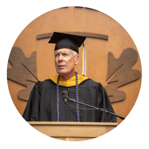 Kerry Carmody wears academic regalia and speaks in front of a Linfield embelm