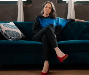 A woman sits on a blue velvet couch, smiling