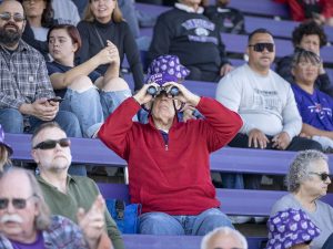 A fan looking through binoculars at the football game during Linfield Homecoming 2024