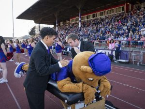 Two people giving Mack the wildcat chiropractic treatment at the football game during Linfield Homecoming 2024