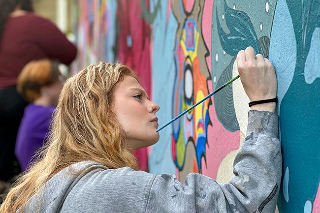 Student paints details on a large-scale mural.