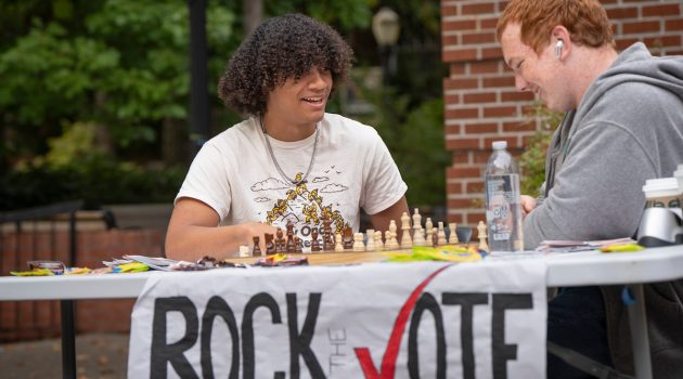 Two students play chess while sitting at a Rock the VOte table