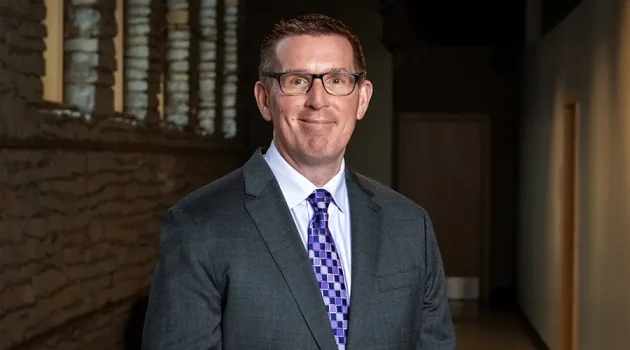 A man in a purple tie stands next to a wall made of stone