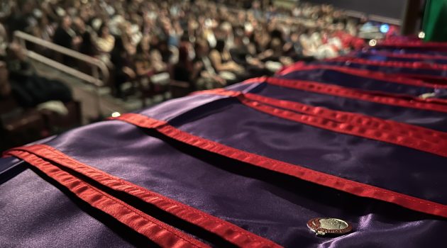 Linfield School of Nursing pins on purple and red graduation stoles, with an auditorium full of people in the background.