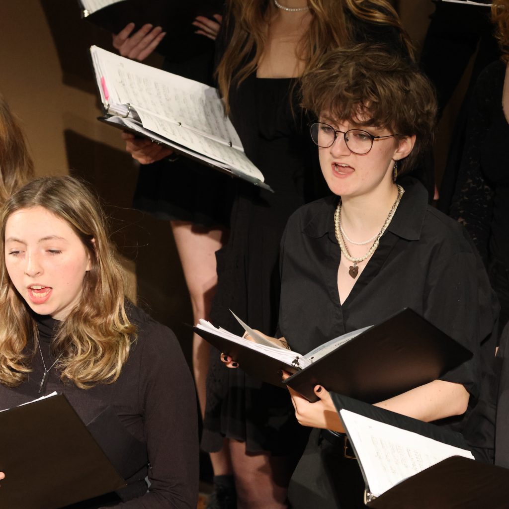 Choir members perform a song while holding sheet music binders