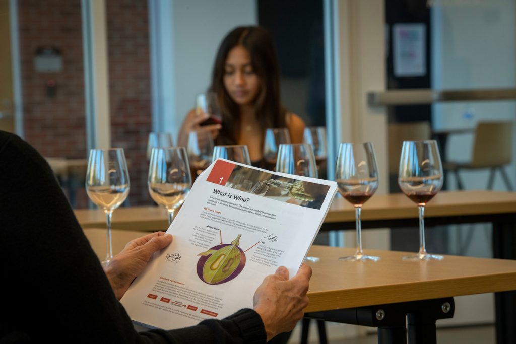 Worksheet about grape anatomy in foreground with woman smelling wine in the background at WSET class.
