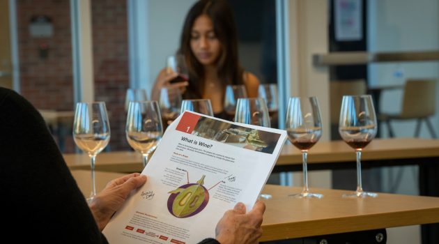 Worksheet about grape anatomy in foreground with woman smelling wine in the background at WSET class.