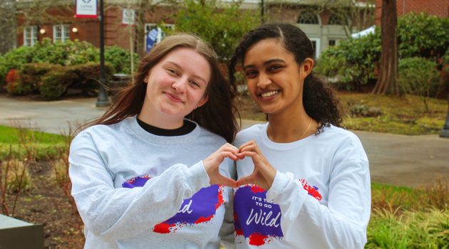 two students wearing Linfield giving day shirts pose with hands in heart shape