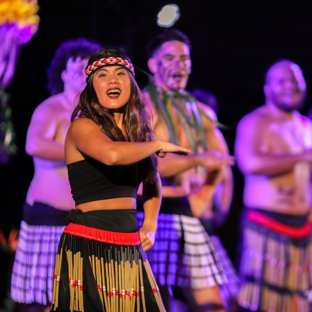 Female dancer performs in front of row of male dancers at 2024 luau