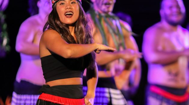 Female dancer performs in front of row of male dancers at 2024 luau