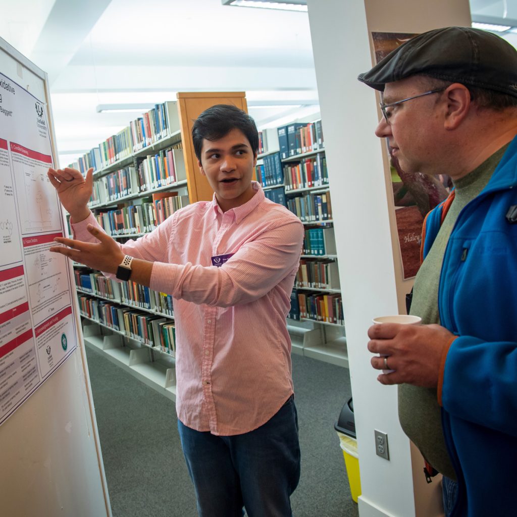 A student presents his academic poster to a passerby.