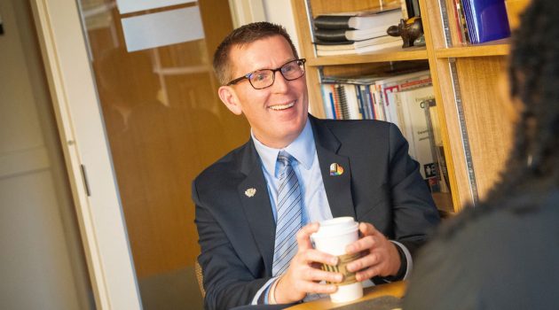 Mark Blegen sits at a table talking to a colleague