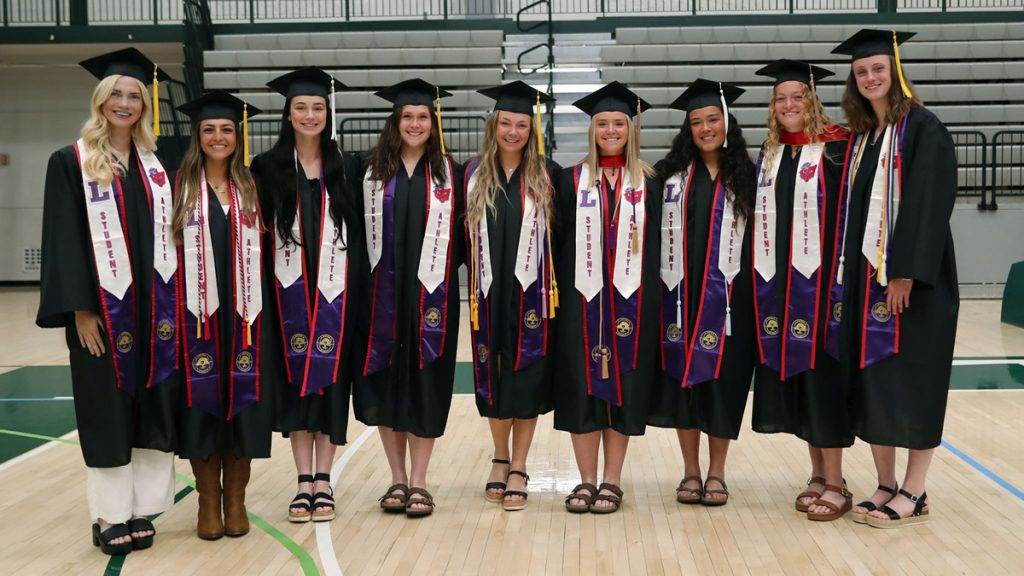 Nine softball players - and Linfield graduates - pose in a line in the gym at Illinois Wesleyan after the mini graduation ceremony.