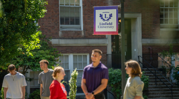 Students in foreground and background in front of building on McMinnville campus. Linfield University pole banner on center.
