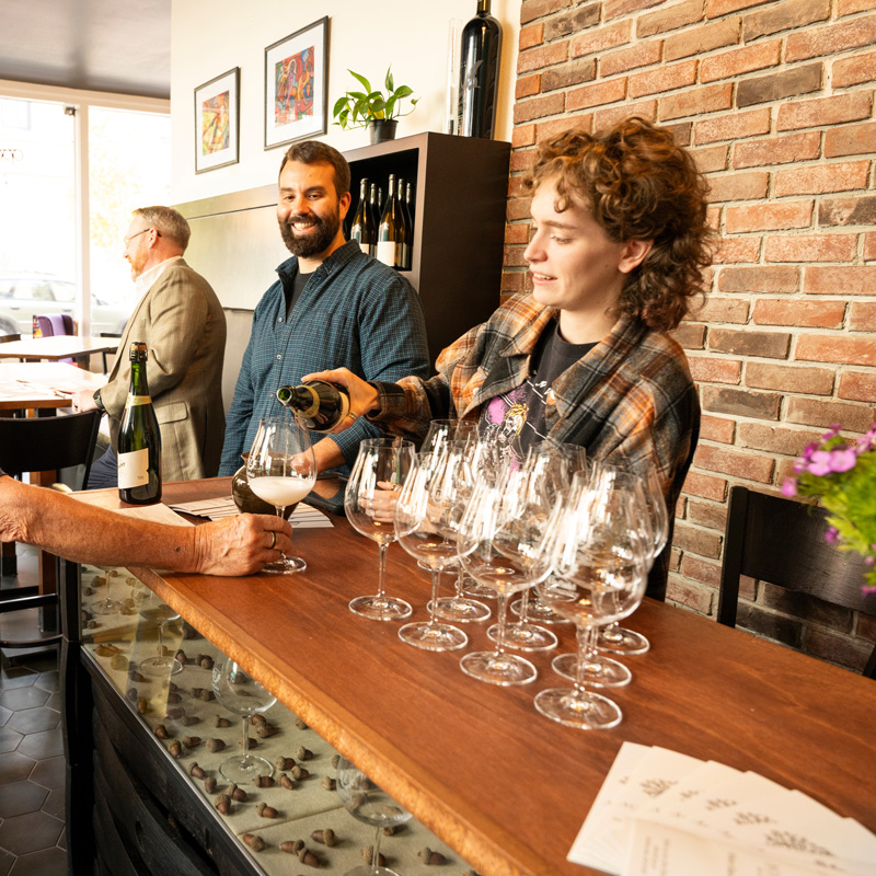 Student worker pours wine at a bar in Acorn to Oak