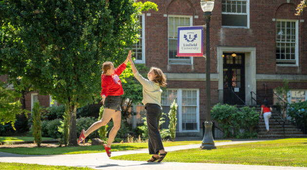 Two students jump and give eachother a high five on campus