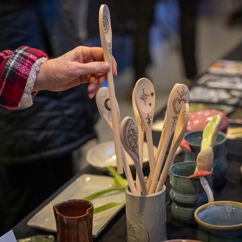 buyer pulls an engraved wooden spoon out of a crock at the Maker's Market.