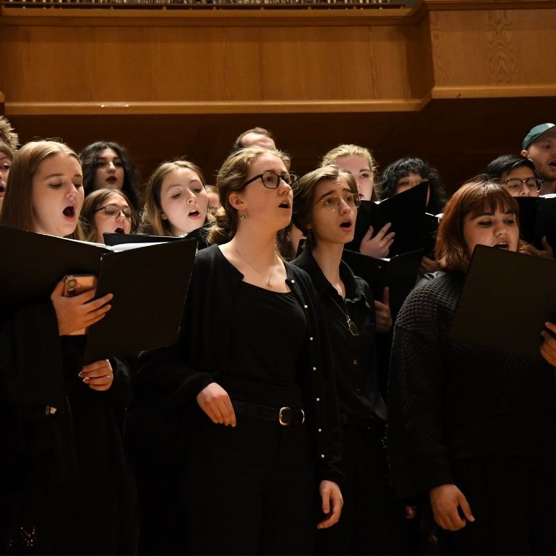 A large group of members from the Linfield choir sing on risers.