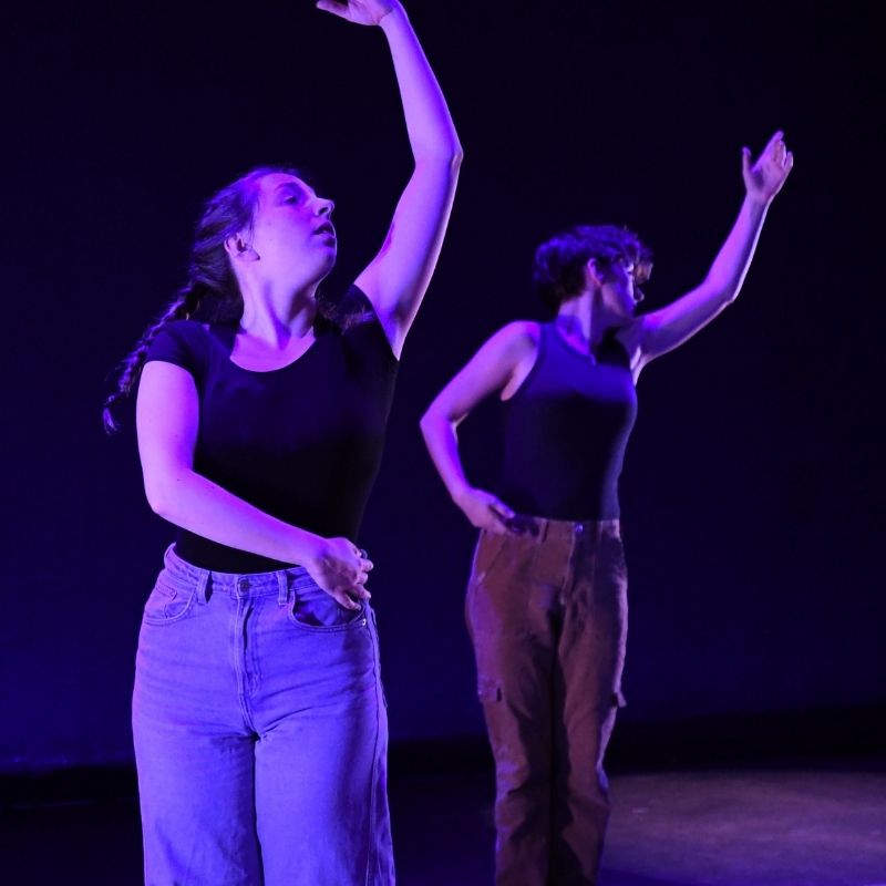 Two dancers perform on stage under a blue light.