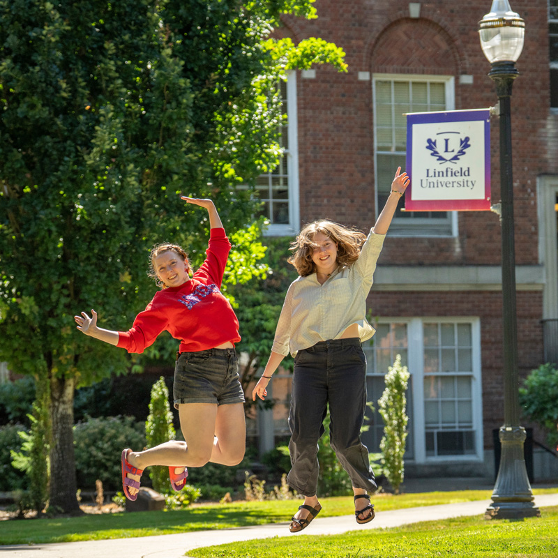 two students jump in the air outside a campus building