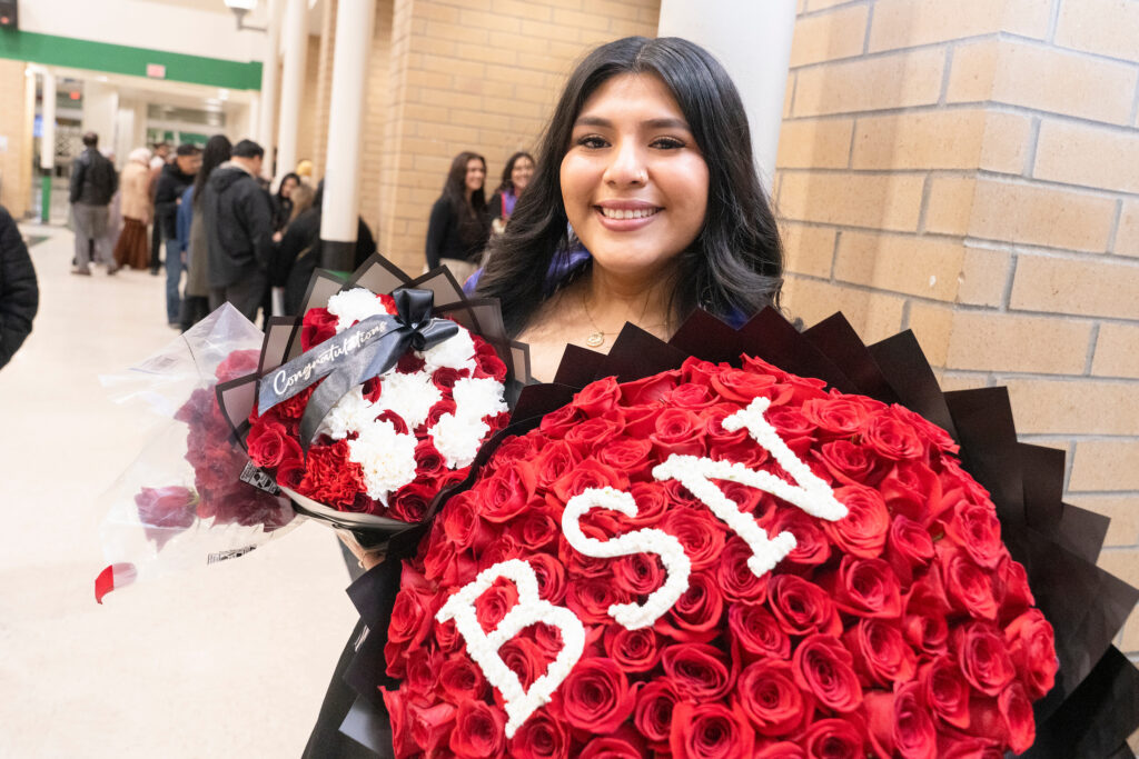 Female graduate holds roses with letters BSN in them.