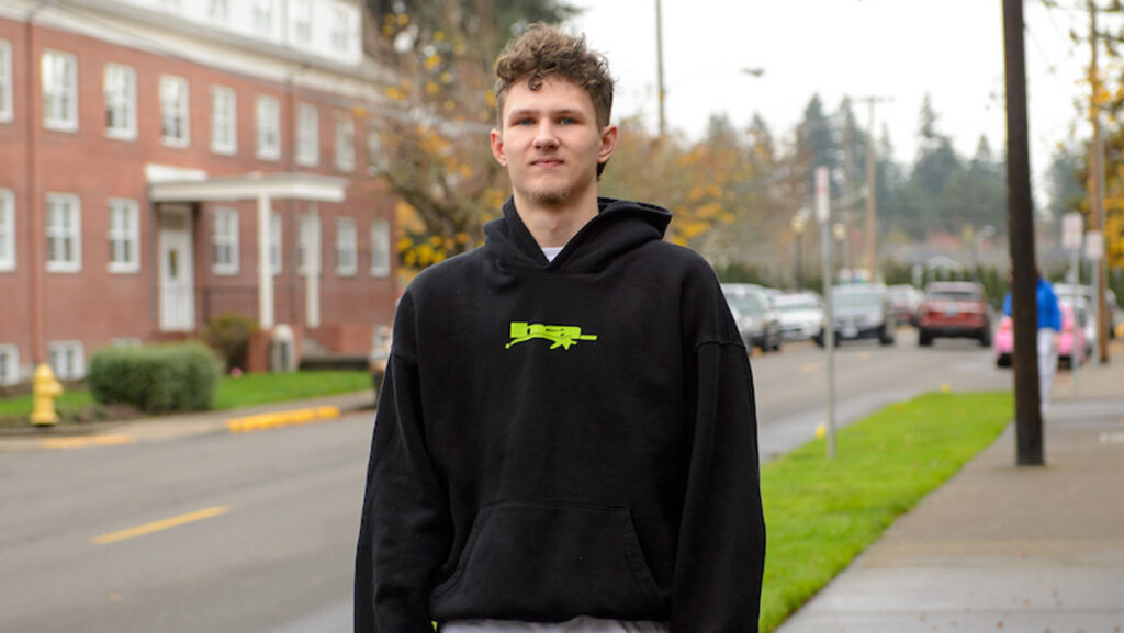 Kris walks down a campus sidewalk with the athletic department in the background