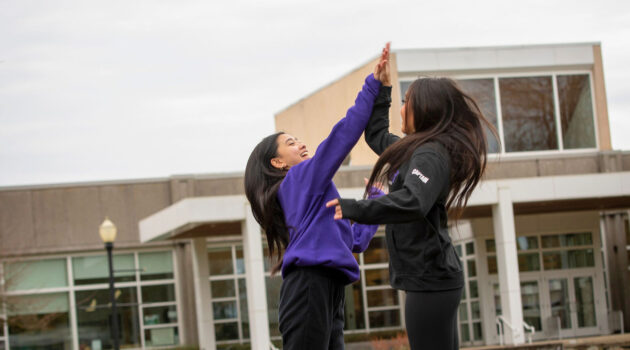 Two students give a jumping high five outside NIcholson Library
