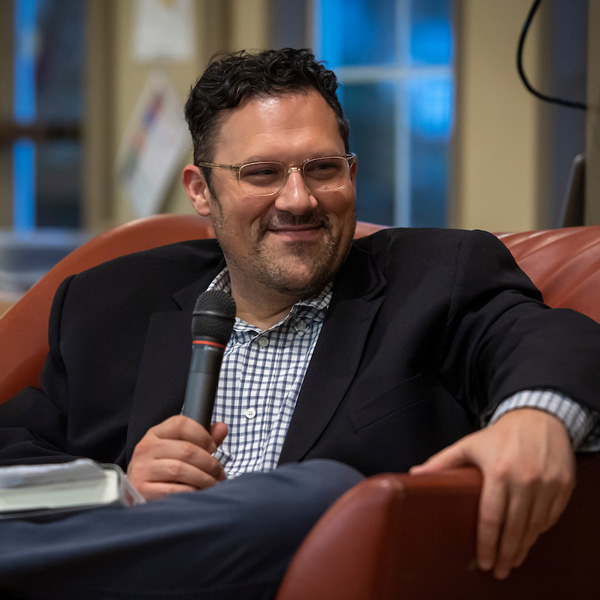 Nick Buccola, smiling, sits in armchair with a microphone