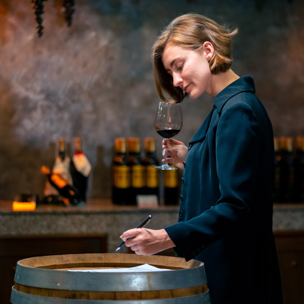 Woman holds a wine glass while looking down at a paper on top of a wine barrel